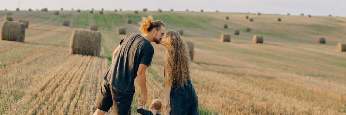 A couple with their child enjoy a sunny day in a wheat field, symbolizing love and joy.